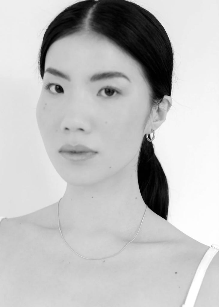 Black and white portrait of a person wearing small silver hoop earrings on a plain background